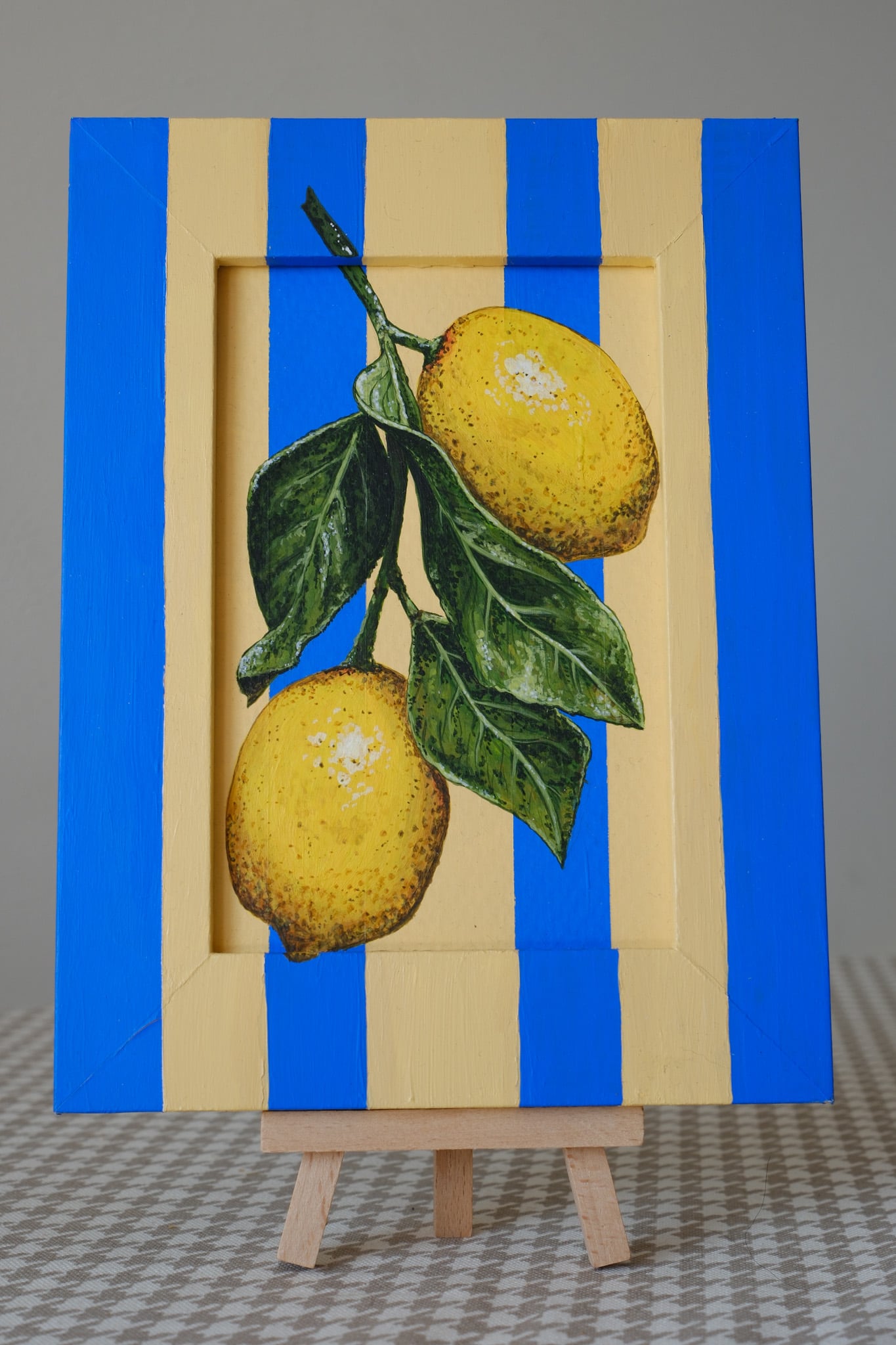 Original lemon gouache painting on a blue and cream striped panel displayed on a small wooden easel.