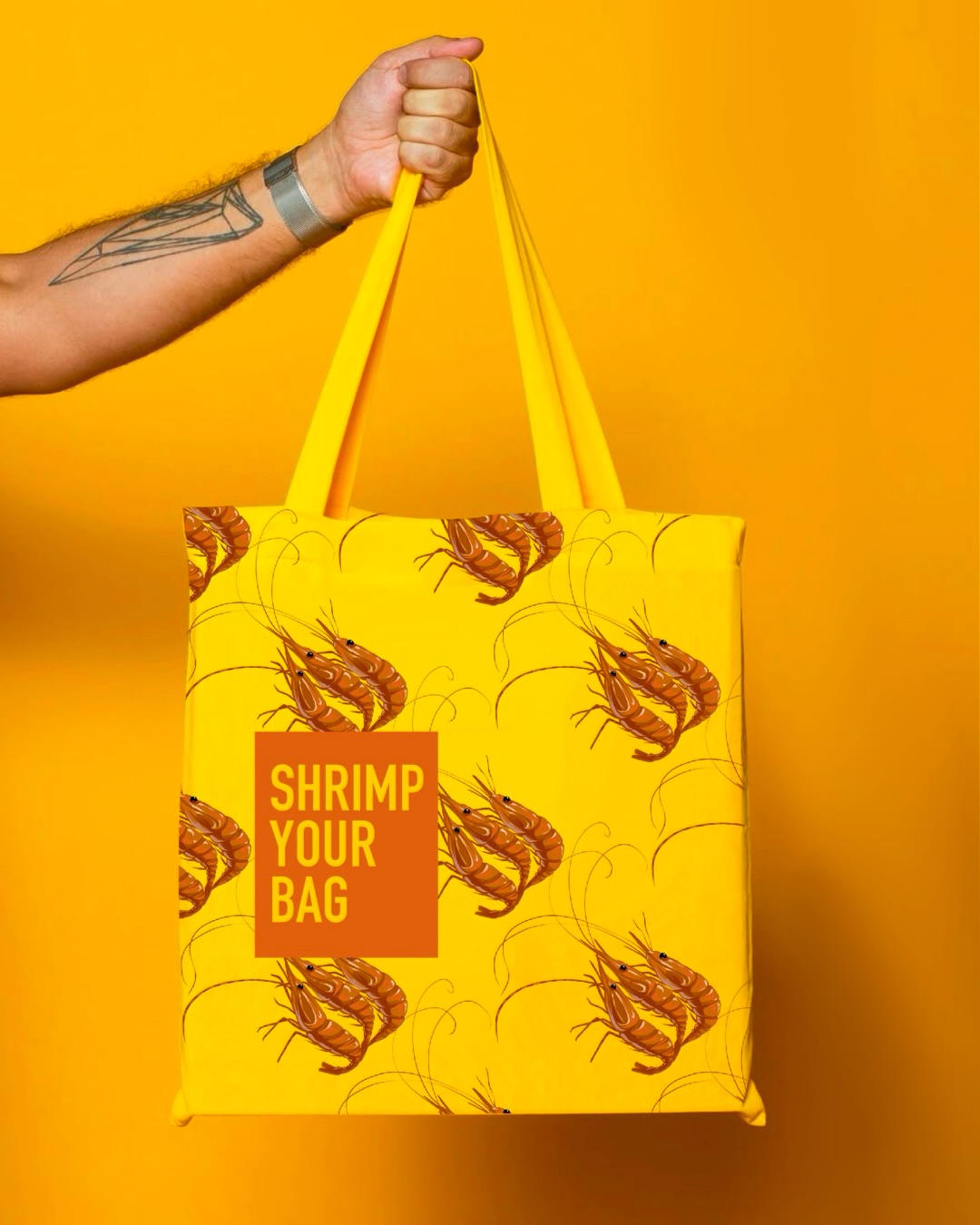Bright yellow tote bag mockup covered in repeating shrimp illustrations with an orange label reading Shrimp Your Bag.