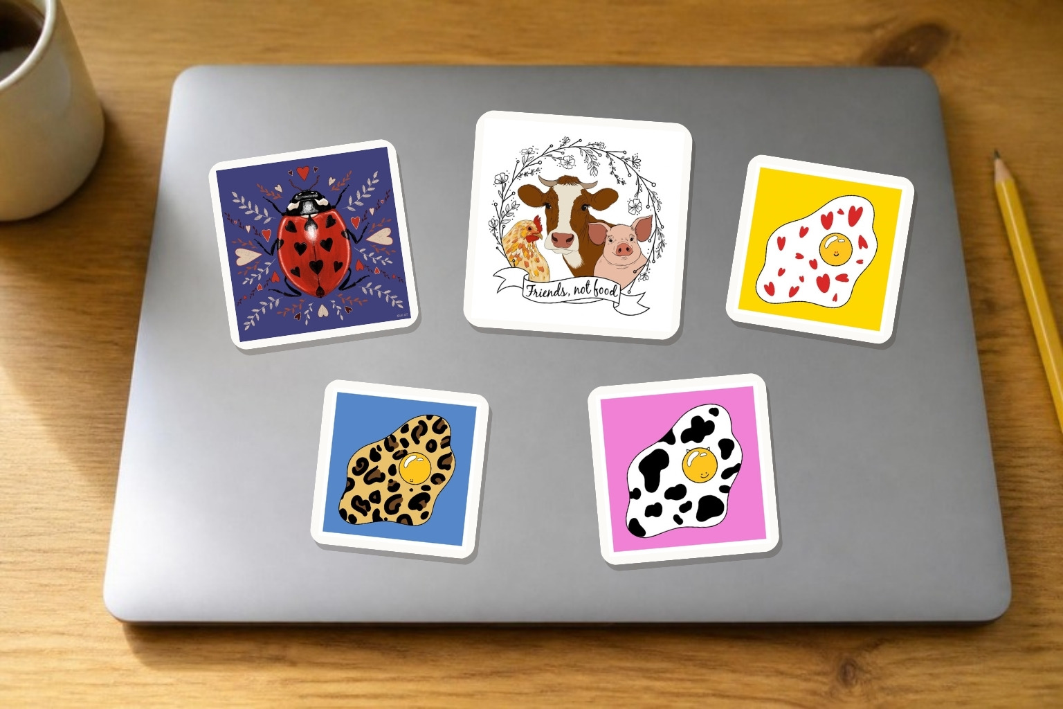 Mockup of Adelya's ladybug, Friends not food and fried egg designs as vinyl stickers on a laptop lid